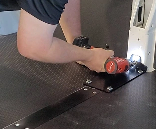 A worker attaching flooring to a van frame